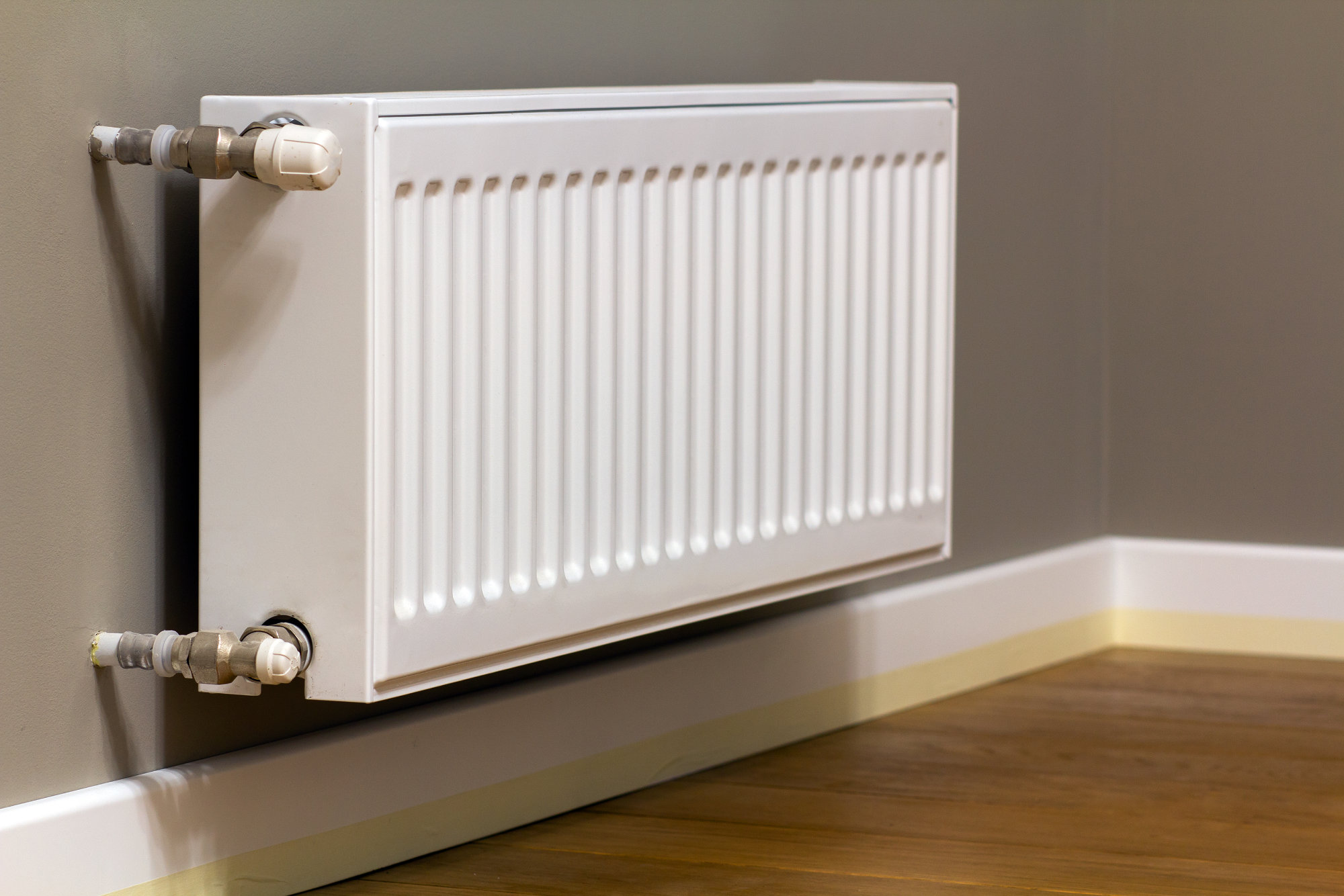 White metal heating radiator mounted on gray wall inside a room.